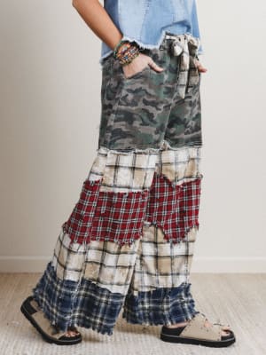 Person wearing patchwork pants with camouflage, plaid, and denim patterns on a neutral background.