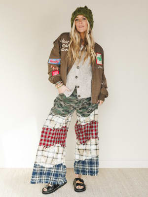 Person wearing a brown jacket with patches, a green beanie, and plaid pants on a white background