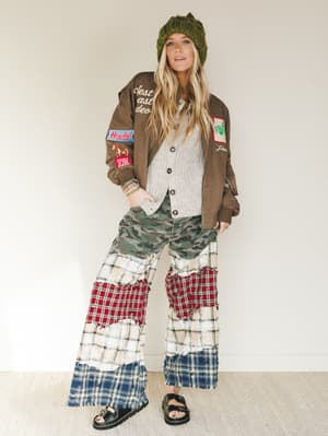 Person wearing a brown jacket with patches, a green beanie, and plaid pants on a white background