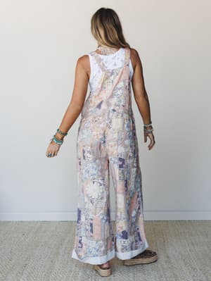 Shot from behind, a model wears wide-leg patchwork floral overalls layered over a white crochet tank, styled with espadrille platform sandals and stacked turquoise bracelets — relaxed, expressive, and very much a 'found this at a vintage market' kind