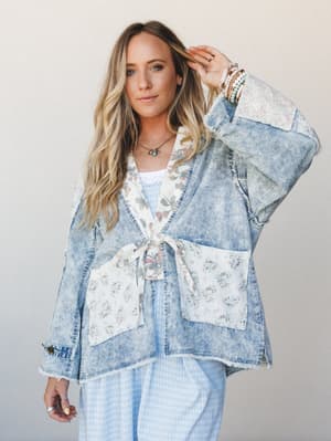 A relaxed denim jacket with floral patchwork panels and a front tie closure layered over a light blue gingham set — the kind of piece that looks like it was always yours.