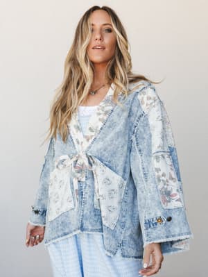 A relaxed, lived-in denim jacket with floral patchwork panels and a tie-front waist, styled over a light blue gingham bottom — the kind of piece that looks like it has a story.