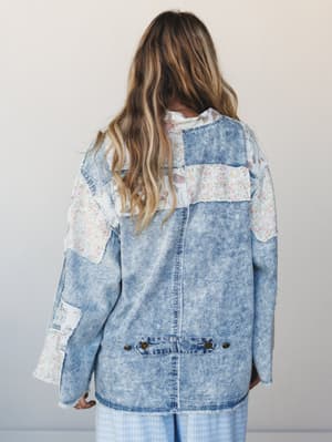 A back-facing model shows off an oversized acid-wash denim jacket pieced together with floral patchwork panels — the kind of jacket that looks like it has a whole backstory.