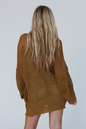 A person with long, wavy blonde hair stands with their back to the camera, wearing the Brenden Knit Netted Cardigan in brown against a plain light background.