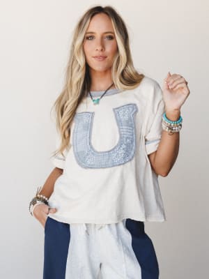 A relaxed, oversized cream tee with a patchwork bandana-print horseshoe appliqué gets styled with navy sweatpants and a stack of boho bracelets — the kind of effortless combo that looks like you tried just the right amount.