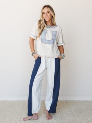 A relaxed, lived-in set styled with a cream oversized tee featuring a patchwork horseshoe appliqué and color-blocked wide-leg pants — layered with turquoise jewelry for that easy boho-western feel.