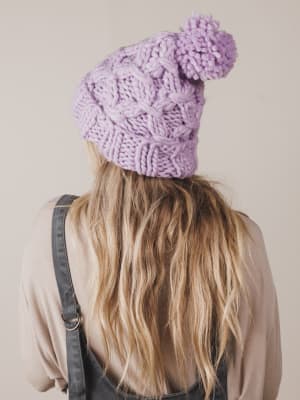 Person wearing a purple knitted beanie with a pom-pom on a plain background