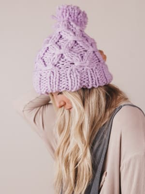 Person wearing a purple knitted beanie with a pom-pom on a plain background