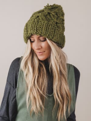 Woman wearing a green knitted beanie and vest against a plain background