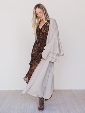 Woman wearing a patterned dress with a beige cardigan against a white background