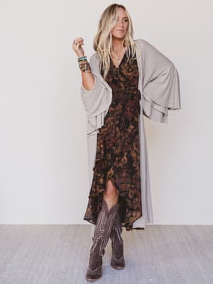 Woman wearing a patterned dress with a cardigan and boots against a white background