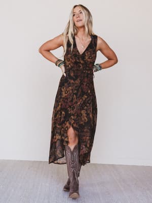 Woman wearing a patterned dress and cowboy boots against a plain background