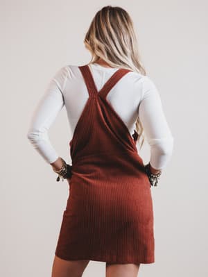 Person wearing a brown ribbed dress with suspenders on a plain background