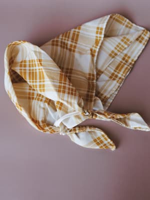 A mustard and cream plaid bandana tied in a loose knot, laid flat against a muted rose background — the kind of little accessory that quietly makes an outfit feel intentional.