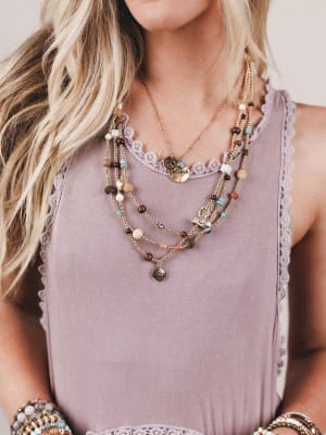 Person wearing a layered necklace with various beads and charms on a light background