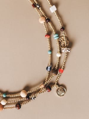 Multistrand beaded necklace with various colored beads and charms on a beige background