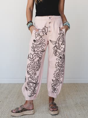 Blush pink wide-leg jogger pants covered in bold black floral embroidery steal the show here — paired with a black smocked crop top, stacked beaded bracelets, and platform espadrille sandals for a look that's equal parts artsy and effortless.