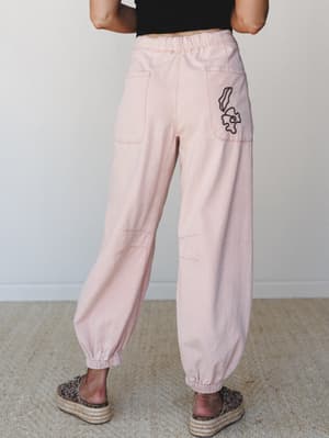Shot from behind, these soft blush jogger-style pants with embroidered pocket detail are styled with a black crop top and leopard espadrille platforms — easy, expressive, and very much the kind of outfit you'd actually wear on a good day.