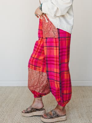 Bold pink plaid harem pants with lace patchwork panels styled with a cream sweatshirt and leopard print platform sandals — the kind of outfit that commits fully and makes it look easy.