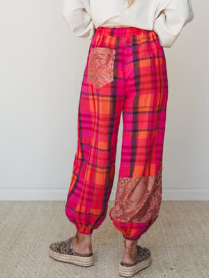 Shot from the back, these bold pink and orange plaid pants with lace patch pockets and banded ankles are styled with a cream sweatshirt and leopard platform espadrilles — relaxed and expressive in equal measure.