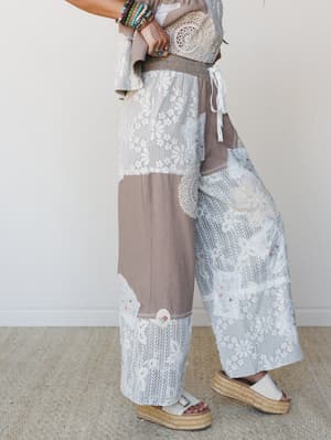 A side-profile shot of wide-leg patchwork pants styled with a matching crochet-trimmed top, stacked bracelets, and platform espadrille sandals — the kind of outfit that looks like it was assembled from the world's most charming vintage quilt.
