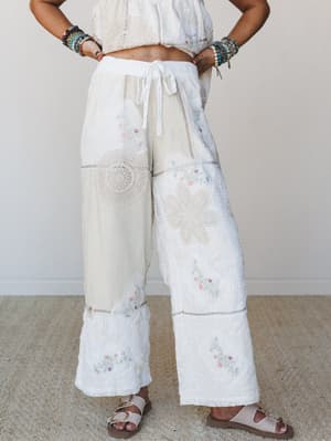 Wide-leg patchwork pants in cream and white styled with a cropped crochet top and stacked bracelets — the kind of outfit that looks like it was assembled lovingly over years, not bought in an afternoon.