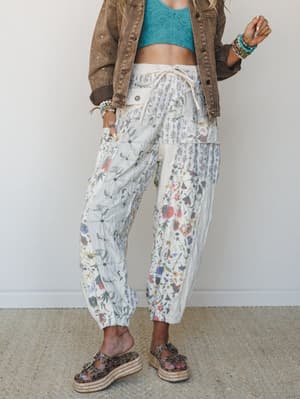 A patchwork floral pant in cream and natural tones styled with a teal lace crop top, washed brown denim jacket, and leopard print platform sandals — the kind of outfit that looks effortless but is clearly doing a lot.