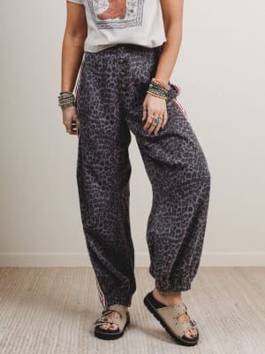 Person wearing leopard print pants and a white top with a colorful design, standing against a plain background.