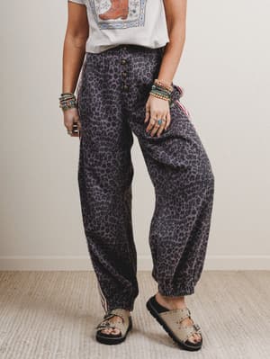 Person wearing leopard print pants and a white top with a colorful design, standing against a plain background.