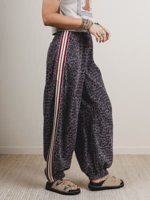 Person wearing leopard print pants with white stripes on a plain background
