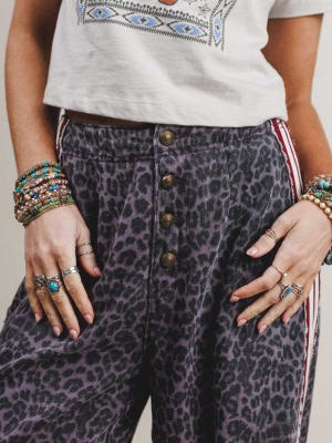 Person wearing a white top with embroidery and leopard print pants with buttons.