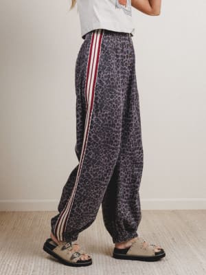 Person wearing leopard print pants with red stripes on a plain background