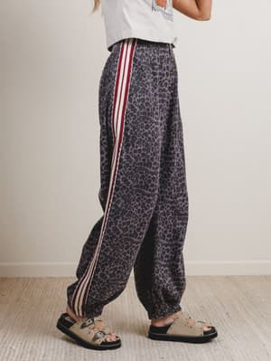 Person wearing leopard print pants with red stripes on a plain background