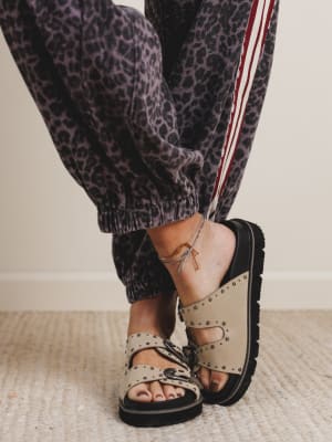 Person wearing leopard print pants and beige sandals with black soles on a neutral background