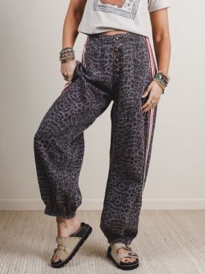 Person wearing leopard print pants with red stripes on a plain background