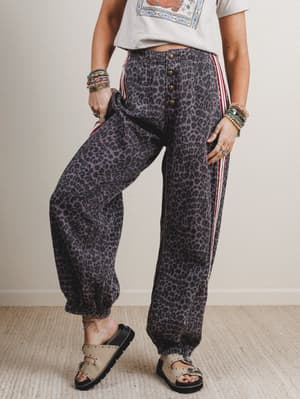 Person wearing leopard print pants with red stripes on a plain background