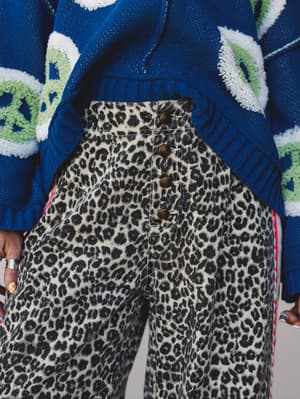 A close-up torso shot of high-waisted leopard print wide-leg pants in sand and charcoal, styled with a bold cobalt blue floral knit sweater — the kind of pattern-mixing that looks intentional rather than accidental.