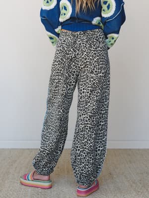 A back-view shot of relaxed leopard print pants with banded ankles, styled with a bold cobalt peace-sign sweater and rainbow platform sandals — playful, expressive, and fully committed to the mix.