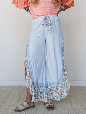 Wide-leg pants in soft baby blue with a textured solid body, floral ruffle hem, and lace trim detailing — styled with a coral top, stacked bracelets, and birkenstock sandals for an effortlessly boho everyday look.