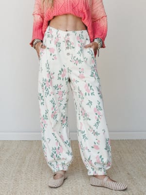 Wide-leg floral pants in cream with soft pink roses and sage green leaves, styled with a cropped coral cable-knit sweater and woven flats — relaxed and pretty in that effortless, garden-party-without-trying way.