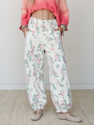 Wide-leg floral pants in cream with soft pink roses and sage green leaves, styled with a cropped coral cable-knit sweater and woven flats — relaxed and pretty in that effortless, garden-party-without-trying way.