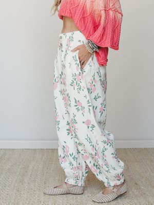 A relaxed, flowy floral pant in cream with pink roses and sage green leaves, styled with a cropped coral cable-knit sweater and woven flat mules — the kind of outfit that looks effortless but was definitely thought about.