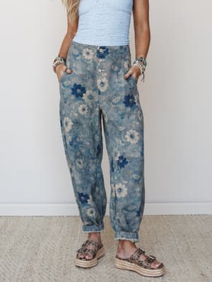 A relaxed, lived-in pair of floral barrel-leg pants in a washed indigo and cream print, styled with a light blue textured crop top, stacked bracelets, and platform espadrille sandals — the kind of outfit that looks like it came together effortlessly