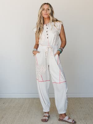 A cream patchwork jumpsuit with floral appliqué, contrast stitching, and a tie waist — worn with Birkenstock sandals and stacked bracelets for an effortlessly personal, boho-everyday kind of vibe.