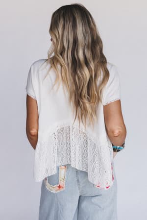 A woman with long wavy blonde hair stands facing away, wearing the Callie Short Sleeve Tee in white and light blue striped jeans, set against a plain white background.