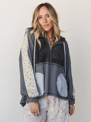 A mixed-media patchwork hoodie in charcoal layers waffle knit, sherpa, floral cotton, and stripe panels into something that feels like your most interesting thrift find — styled with embroidered stripe pants and stacked beaded necklaces for a very li