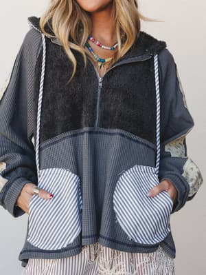 A mixed-media hooded zip-up in charcoal layers sherpa, waffle knit, stripe, and floral patchwork panels — the kind of cozy top that looks like it was assembled from all your favorite textures at once.