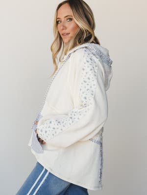 A cream waffle-knit hooded top with floral print and striped contrast panels gives off that perfectly thrown-together, cozy-but-make-it-pretty energy — styled with blue jeans for an effortlessly casual look.