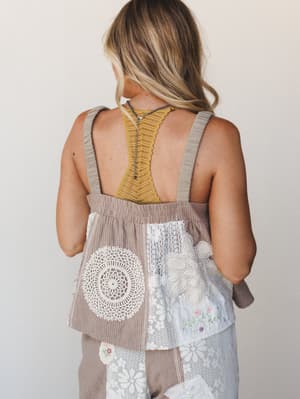 Shot from the back, this model wears a loose woven top with wide straps and a patchwork lower half — doily crochet, lace panels, and floral embroidery all stitched together in the most collected, lived-in way, layered over a mustard racerback bralett