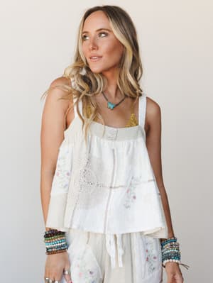 A cream woven patchwork tank top with crochet medallion and floral embroidery details, styled with stacked beaded bracelets and a turquoise pendant necklace — the kind of effortless boho layering that looks like it took zero effort and somehow all th